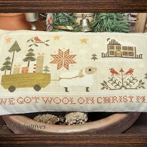 May include: A white pillow with a cross-stitch design featuring a sheep pulling a wagon full of presents, a house, and a star. The text "Ewe got wool on Christmas" is stitched below the design.