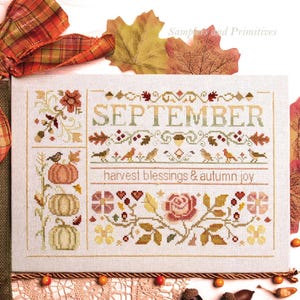 Pode incluir: Um mostruário de ponto cruz retangular em tecido claro com o texto SEPTEMBER e harvest blessings & autumn joy. O design inclui abóboras, pássaros, uma rosa e várias folhas de outono bordadas em tons de laranja, castanho e verde.