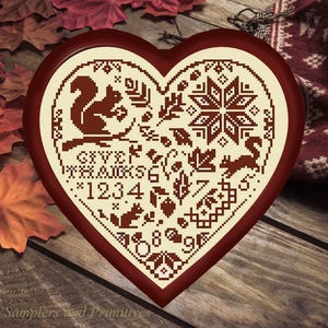 May include: A heart-shaped wooden plaque featuring a cream-coloured cross-stitch pattern with dark brown motifs including squirrels, autumn leaves, acorns, a star, and the text "GIVE THANKS" along with the numbers 1, 2, 3, 4, 5, 6, 7, 8, and 9.