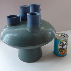 May include: A blue and green ceramic vase with five openings for flowers. The vase is shaped like a mushroom with a wide, flat top and a rounded base.