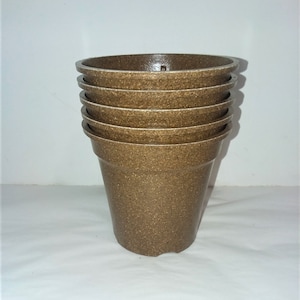May include: A stack of six brown, textured flower pots. The pots are made of a speckled material and have a simple, classic design. The pots are empty and ready for planting. The pots are a neutral color that would complement any plant.