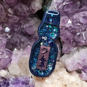 May include: A blue and green glass bottle charm with a white star and glitter design. The bottle has the Japanese word "Ramune" written on it.