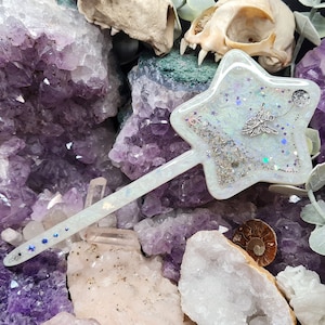 May include: A white star-shaped wand with glitter embedded in the resin. The wand is surrounded by amethyst and clear quartz crystals.
