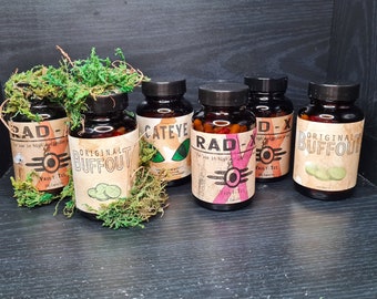 May include: Six small glass bottles with labels and caps. The labels are printed with the words "RAD", "CATEYE", "ORIGINAL BUFFOUT", "D-X", "RAD", and "ORIGINAL BUFFOUT". The bottles are arranged in a row on a dark surface.