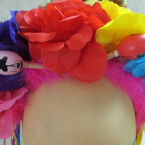 May include: A colorful flower crown with pink, red, yellow, blue, and purple flowers. The crown is decorated with maracas and feathers.