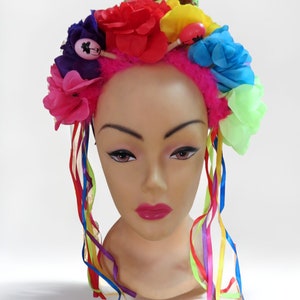 May include: A pink headband with colorful flowers and ribbons. The headband is decorated with a variety of flowers in pink, red, blue, yellow, and green. The ribbons are rainbow colored and hang down from the headband.