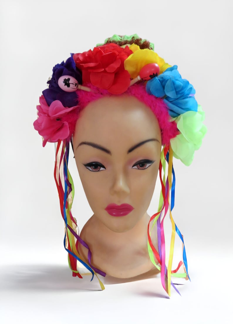 May include: A pink headband with colorful flowers and ribbons. The headband is decorated with a variety of flowers in pink, red, blue, yellow, and green. The ribbons are rainbow colored and hang down from the headband.
