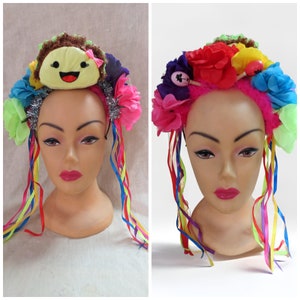 May include: A colorful headband with a variety of flowers, ribbons, and a plush taco with a smiling face. The headband is pink and has a fuzzy texture.