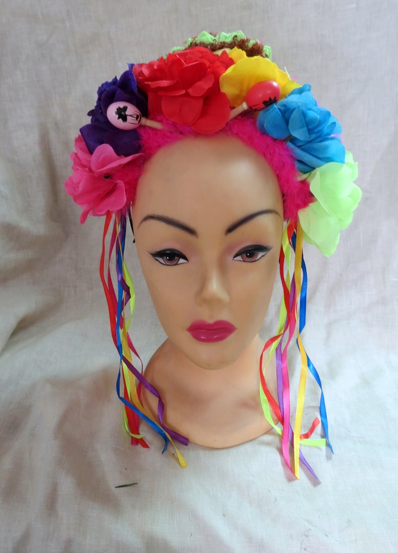 May include: A colorful flower crown headband with pink, red, blue, purple, yellow, and green flowers. The headband has long, colorful ribbons attached to it.