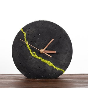 Peut inclure: Une horloge en béton noir avec un motif de mousse verte et des aiguilles en cuivre.