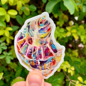 May include: A colorful seashell sticker with a white background. The shell is painted with a variety of colors, including blue, green, yellow, red, and purple.