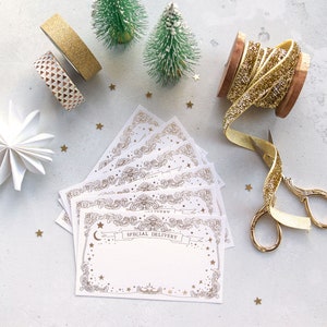 May include: A collection of white cards with gold ornate borders and the text "SPECIAL DELIVERY". The cards are surrounded by gold stars, decorative tape, miniature green Christmas trees, and gold ribbon.