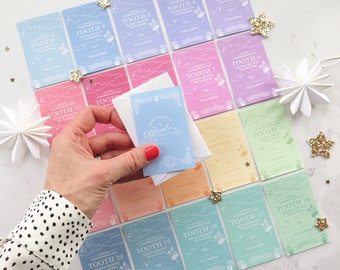 May include: A set of 20 colorful tooth fairy cards with a whimsical design featuring clouds, stars, and mushrooms. Each card is labeled with a tooth number, from 1 to 20. The cards are arranged in a grid pattern on a white surface. A hand is holding a small envelope with a tooth fairy design.
