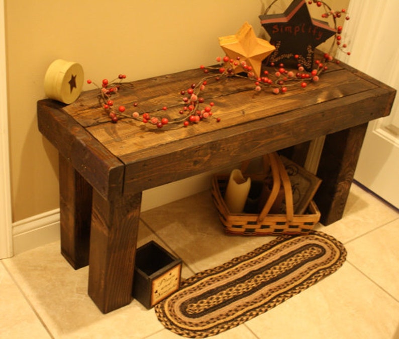 May include: A rustic, dark-stained wooden bench with a slatted top. The bench features a star-shaped decoration, a small basket, and a decorative garland. A small rug is placed in front of the bench.