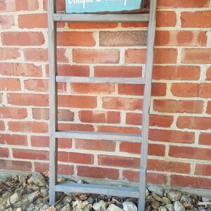 May include: A gray wooden ladder shelf with four shelves. The shelf has a sign that says "Unique Primtiques" in white lettering on a light blue background.