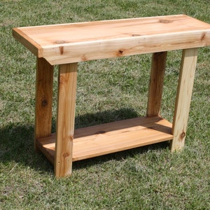 May include: A wooden table with a natural finish and a single shelf. The table is made of unfinished wood and has a rustic look.