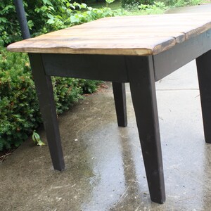 May include: A small wooden table with a black painted base and a natural wood top. The table has four legs and a rectangular top.
