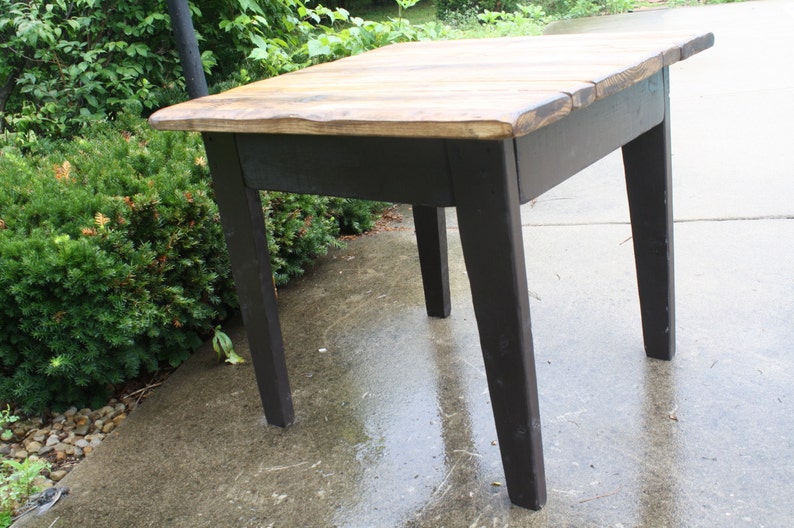 May include: A small wooden table with a black painted base and a natural wood top. The table has four legs and a rectangular top.