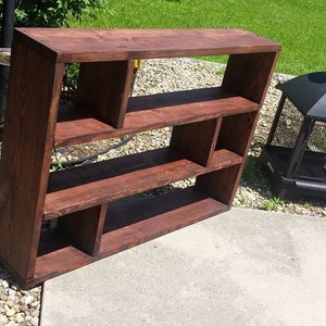 May include: A dark brown wooden shelf unit with multiple open shelves and cubbyholes. The shelf unit is made of solid wood and has a rustic look.