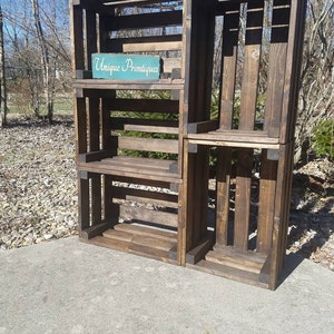 May include: A wooden shelf unit made from repurposed crates. The shelf unit has four shelves and is stained a dark brown color. The shelf unit has a sign that says "Unique Primtiques".