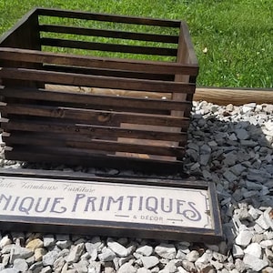 May include: A rustic wooden crate with a sign that reads "Rustic Farmhouse Furniture Unique Primitives & Decor" on a bed of gray gravel.