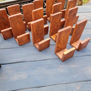 May include: A collection of twelve L-shaped wooden stands with a medium brown stained finish. Each stand features a vertical back panel and a smaller horizontal base piece, designed to hold items upright. The wood grain is visible throughout.