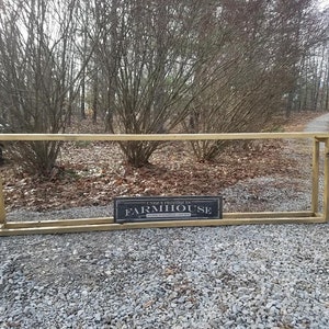 May include: A wooden frame with a sign that reads "Unique Farmhouse" in black lettering on a white background. The frame is lying on a gravel surface.