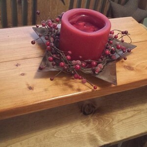 May include: A wooden table with a red candle and a decorative berry wreath on top. The table is made of natural wood and has a rustic look.