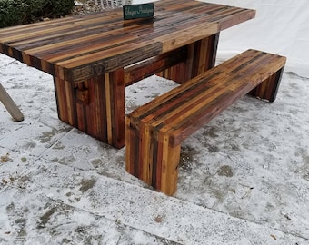 May include: A rustic wooden table and bench set made from reclaimed wood. The table has a long, rectangular top with a variety of wood colors and textures. The bench is also made from reclaimed wood and has a simple, rectangular design. The set is perfect for outdoor dining or entertaining.
