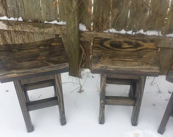 May include: Three dark brown wooden stools with a rustic finish. The stools have a simple design with a rectangular seat and a single support bar.