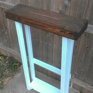 May include: A small, wooden table with a dark brown top and white painted legs. The table has a single shelf.