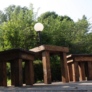 May include: Three wooden stools with a rustic finish, arranged in a row. The stools are made of reclaimed wood and have a natural, weathered look. A white globe light is visible in the background.