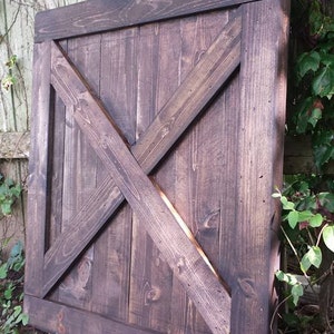 May include: A dark brown wooden door with a diagonal X-shaped design. The door is closed and has a sign above it that reads "Unique Primitives".