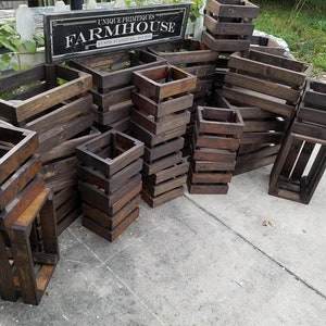 May include: A collection of wooden crates stacked in various sizes and configurations. The crates are made of dark brown wood and have a rustic appearance. The crates are arranged in a way that suggests they are being used for storage or display.
