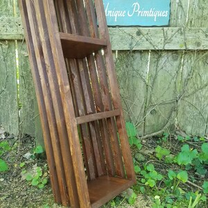 May include: A dark brown wooden shelf unit with three shelves. The shelf unit is made of reclaimed wood and has a rustic look. The shelf unit is leaning against a wooden fence.