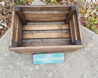 May include: A dark brown wooden crate with a light brown stain. The crate has a sign on the front that says "Unique Primtiques".