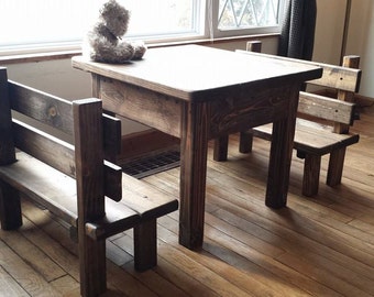 May include: A rustic, wooden children's table and two benches set. The furniture is made of stained wood, with a natural finish. A small teddy bear sits on the table. The table measures approximately 76 cm long.