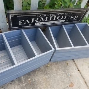 May include: Two gray wooden storage boxes with three compartments each. The boxes are made of reclaimed wood and have a rustic farmhouse style. The boxes are sitting on a concrete surface in front of a black sign that reads "Unique Primitives Farmhouse Rustic Furniture Est. 2010".