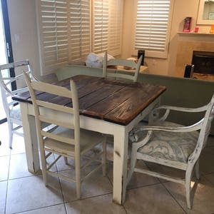 May include: A white farmhouse style dining table with a dark wood top and four chairs. The chairs are painted white with distressed paint and have a light blue and white patterned fabric seat.