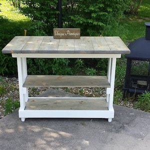 May include: A white and gray wooden console table with two shelves. The table has a distressed finish and is labeled "Unique Primitives".