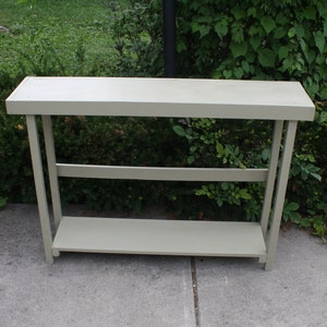 May include: A light gray wooden console table with two shelves. The table has a simple design with straight lines and a rectangular shape.