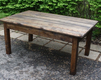 May include: A rustic wooden table with a dark brown stain. The table has a rectangular top and four legs. The table is made of reclaimed wood and has a distressed finish.