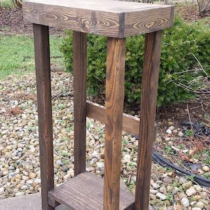May include: A rustic wooden side table with a dark brown stain. The table has a single shelf and is made of reclaimed wood.