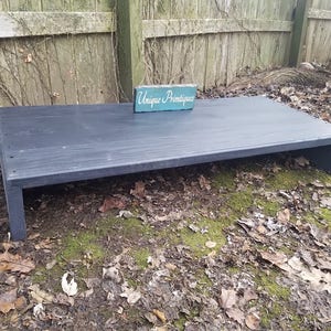 May include: A black wooden platform with a raised edge and a small wooden sign that reads "Unique Primitive" on top.