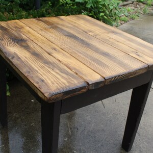 May include: A rustic wooden table with a dark stained top and black painted legs. The table top is made of reclaimed wood planks with a natural wood grain.