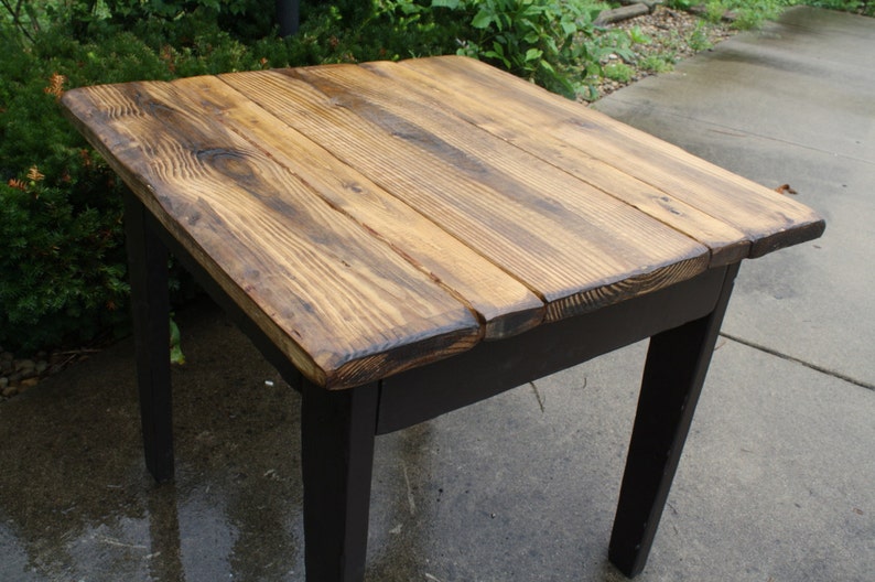 May include: A rustic wooden table with a dark stained top and black painted legs. The table top is made of reclaimed wood planks with a natural wood grain.