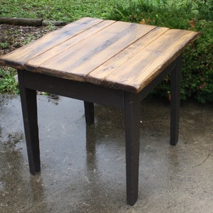 May include: A small wooden table with a dark brown stained top and black painted legs. The table top is made of reclaimed wood planks.