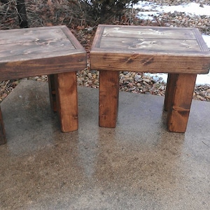 May include: Two rustic wooden stools with a dark brown stain. The stools are made of reclaimed wood and have a simple, farmhouse style.
