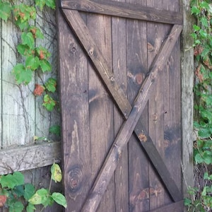 May include: A dark brown wooden barn door with a diagonal X-shaped design. The door is made of reclaimed wood and has a rustic look.