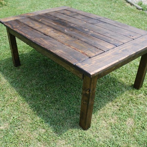 May include: A rectangular wooden table with a dark brown stained finish. The tabletop is constructed from several horizontal planks framed by a border, supported by four sturdy, straight legs. The wood grain is visible throughout the surface.